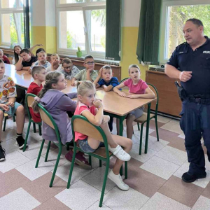 Policjant tłumaczy uczniom zasady bezpiecznego poruszania się po drodze.