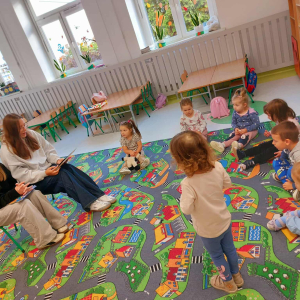 Grupa przedszkolaków z zaciekawieniem słucha bajek, czytanych przez starsze koleżanki.